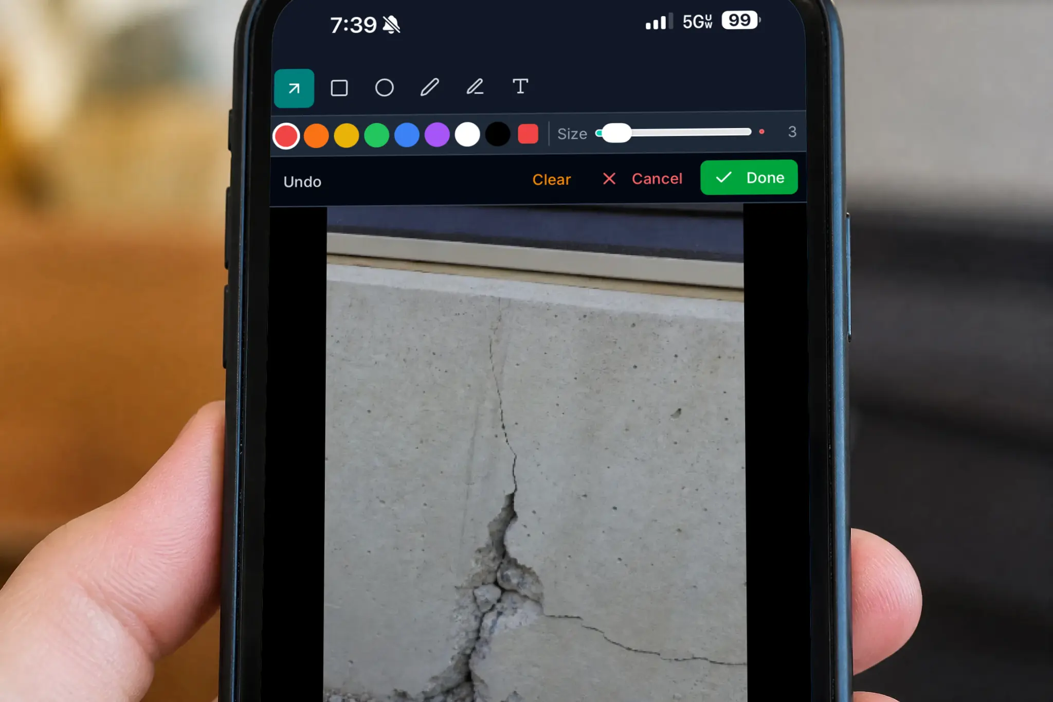CRM With Mobile Photo Editor - CRM With Mobile Image Editor - CRM Software For Contractors — hand holding a phone showing the ContractorCore photo markup editor open on a cracked concrete photo with color and shape tools visible